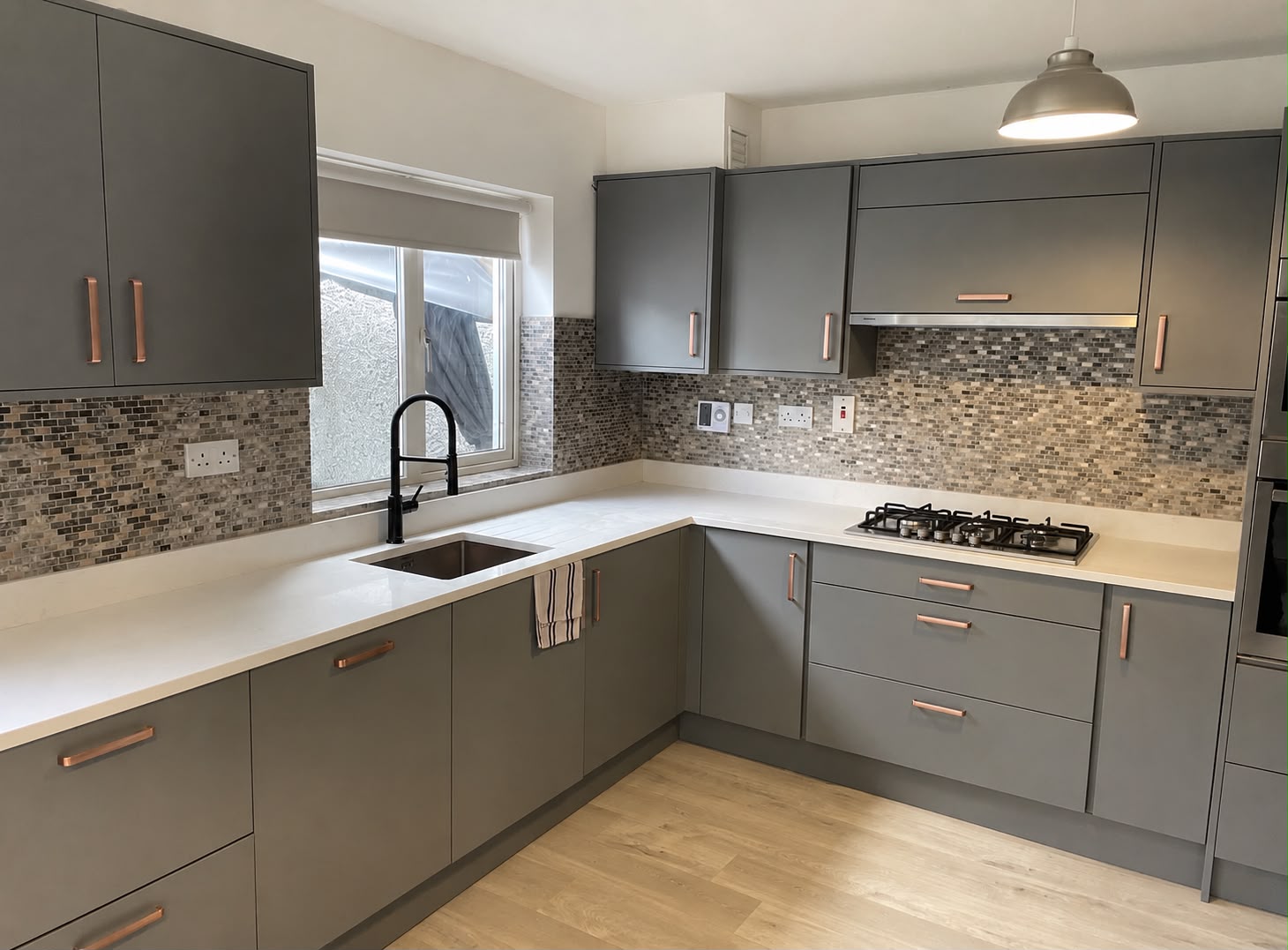 Contemporary L-shaped grey shaker kitchen with copper handles and mosaic tile backsplash