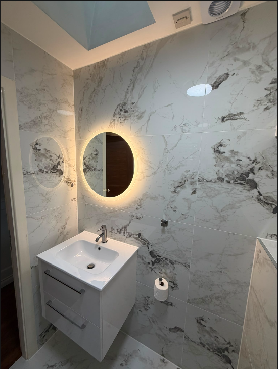 Luxury marble bathroom renovation with backlit circular mirror and white floating vanity